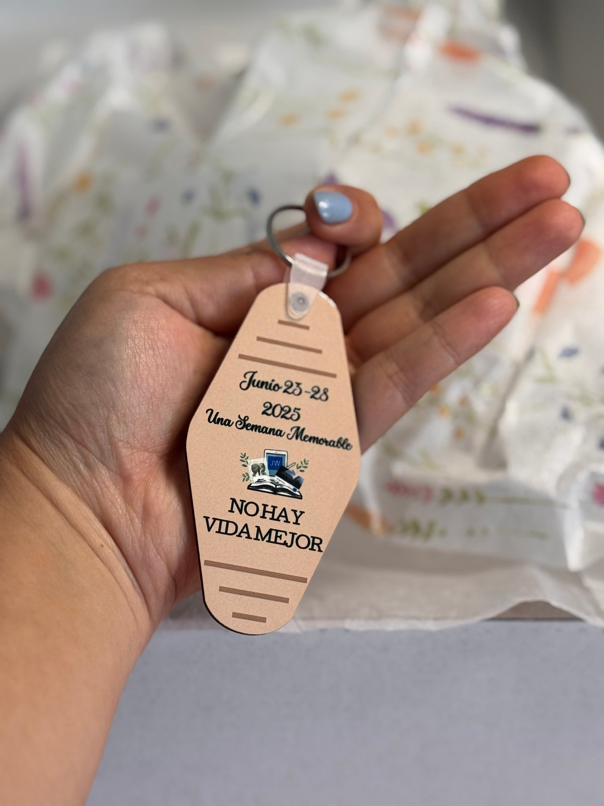 Hand holding a pink motel-style keychain reading "Junio 23-28 2025, Una Semana Memorable, No hay vida mejor"