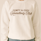 Model wearing a white crewneck embroidered COMFY & COZY Homebody Club in brown