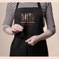 Model wearing a black apron printed with kitchen utensils and "Equipo de Cocina"