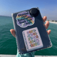 Book fair sticker and a "Don't judge a book by its movie" sticker on an e-reader case, held up by the ocean