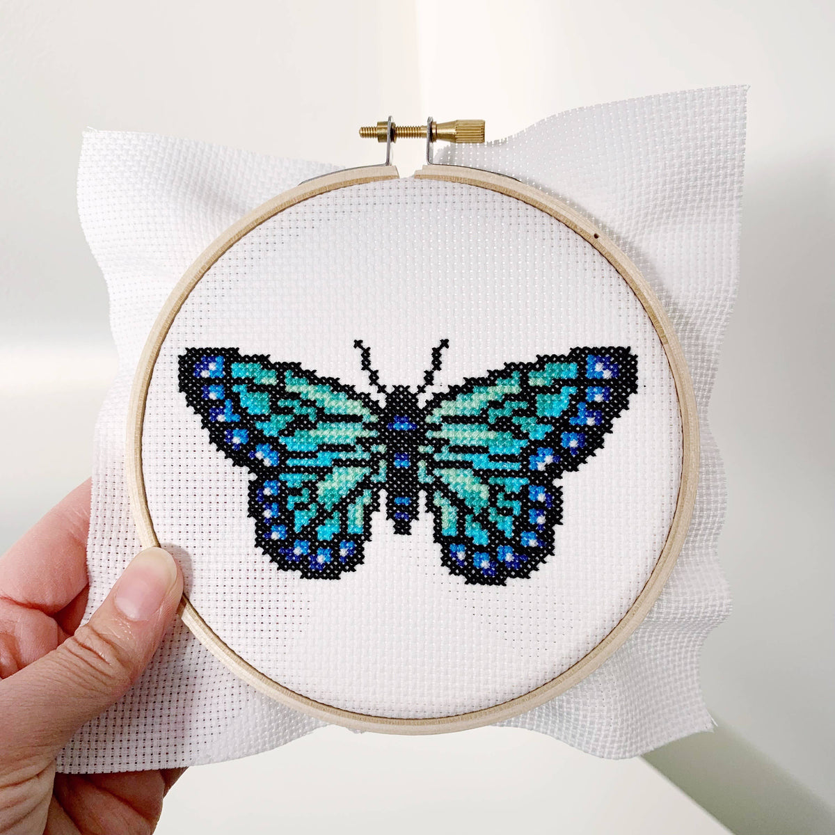 Hand holding the stitched butterfly in its hoop, fabric edges showing