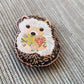 Angled close-up of the hedgehog enamel needle minder with its rose gold outline