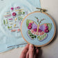 Hand holding the finished butterfly embroidery hoop next to the printed stitch guide