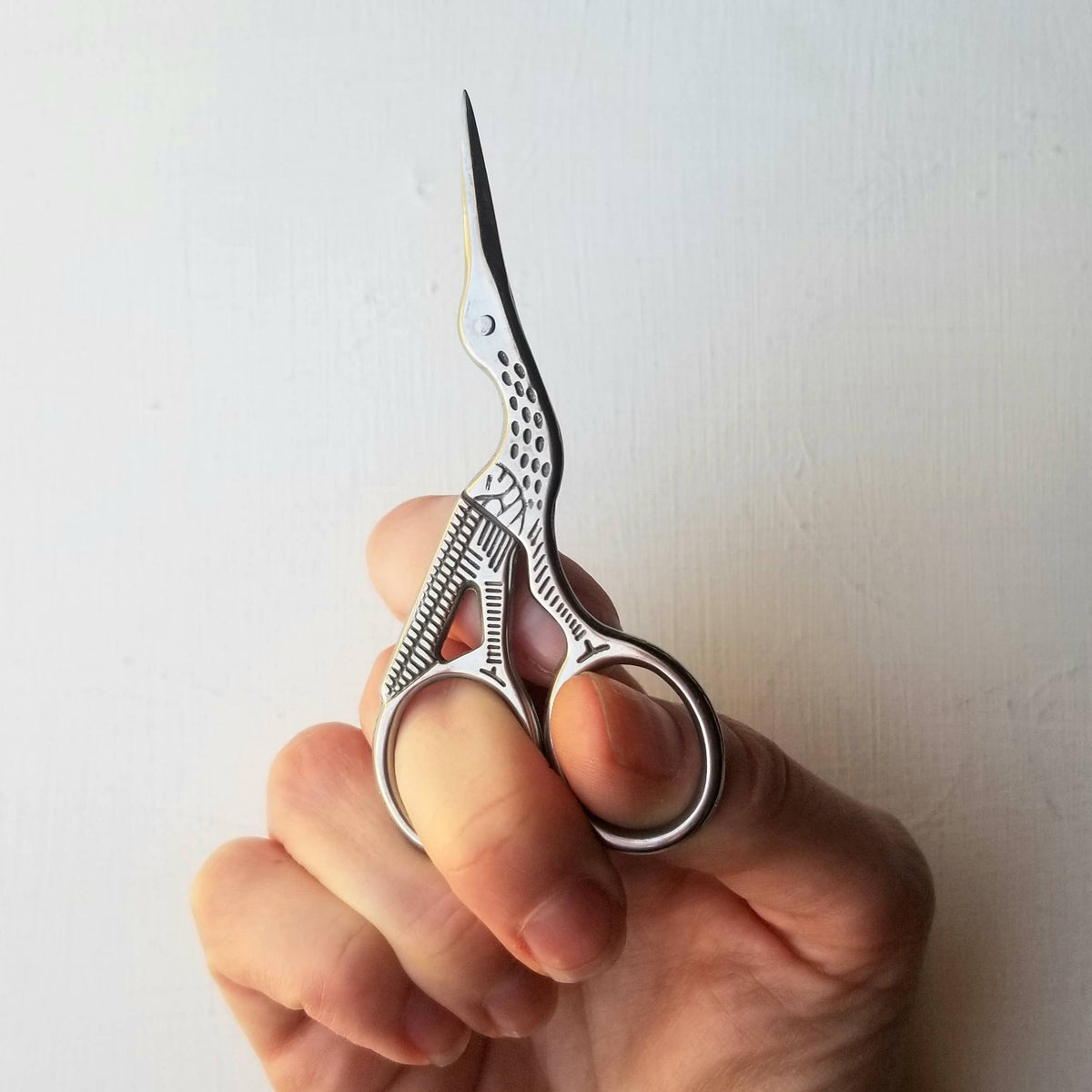 Hand holding silver stork-shaped embroidery scissors