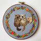 Embroidery hoop of two sea otters in a starfish and flower wreath, with the matching needle minder