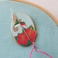 Hummingbird enamel needle minder holding a threaded needle with pink floss on aqua fabric
