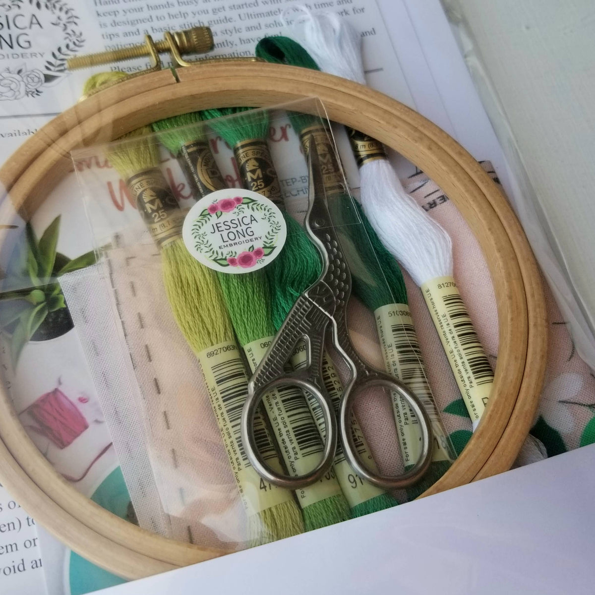Stork scissors resting on green and white DMC floss inside an embroidery hoop